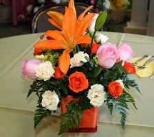 Wedding reception table centerpiece with orange callas, pink roses, orange roses, hydrangea, and green fillers.